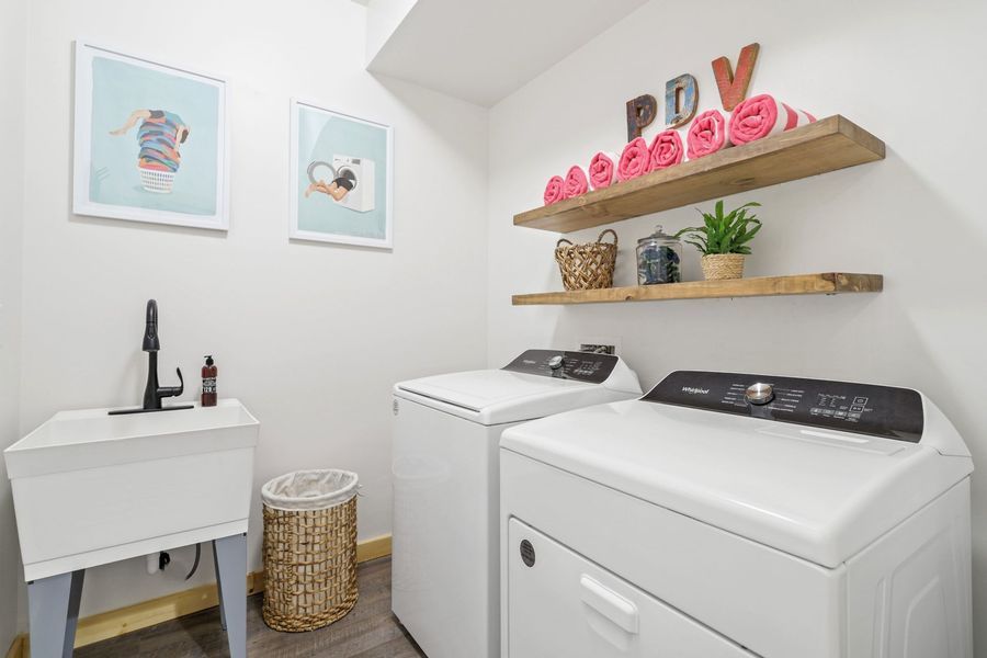 Laundry room with white appliances, shelves with towels, sink, and decorative items.
