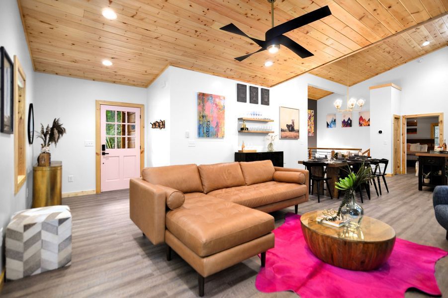 Living room with brown leather sectional, pink door, wood ceiling, and modern art.