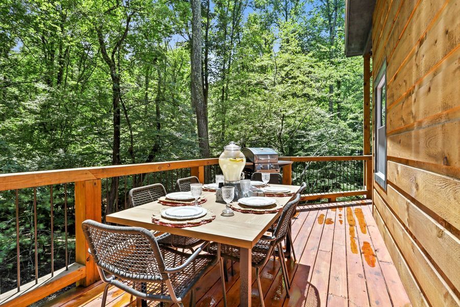 Outdoor dining set on wooden deck with grill and forest view.