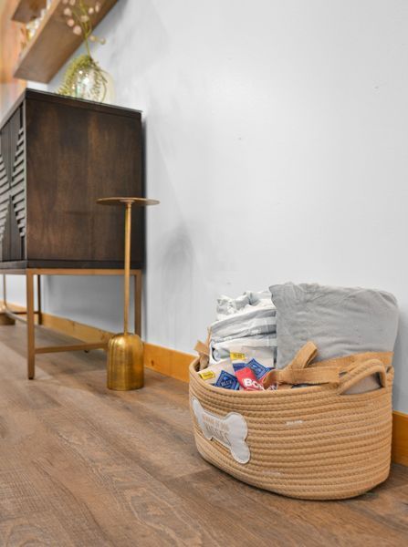 Woven basket with dog supplies next to a mid-century modern cabinet on wood floor.