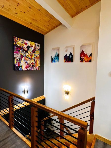 Staircase with wood banisters, metal rods, and colorful artwork on gray and white walls.
