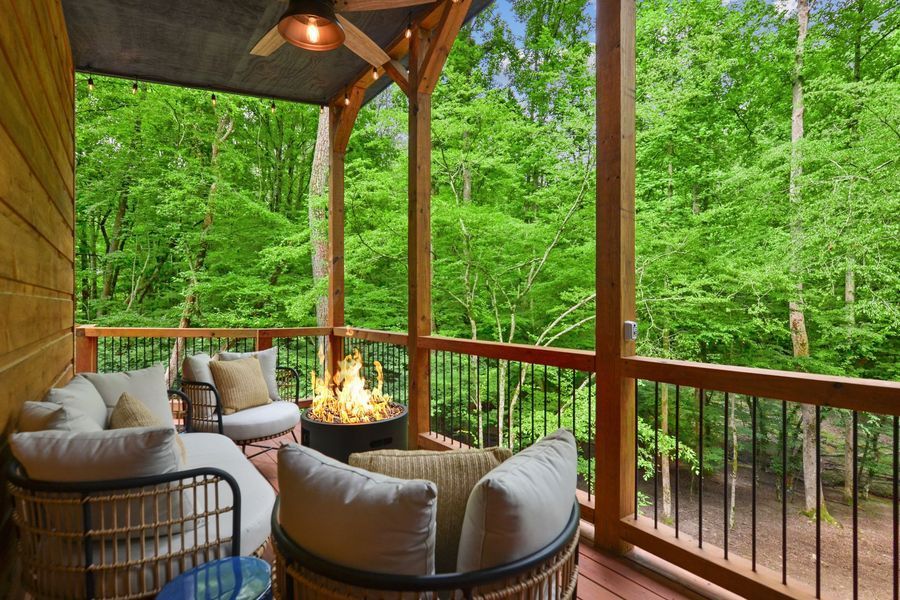Cozy porch with seating, fire pit, and forest backdrop; natural wood and green foliage.
