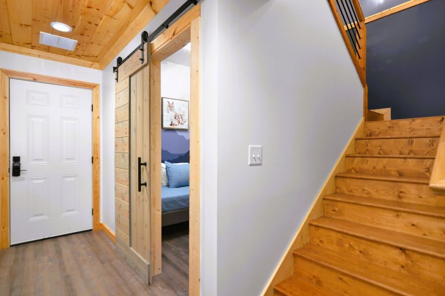 Hallway with wooden stairs, a sliding barn door to a bedroom, and a white door.