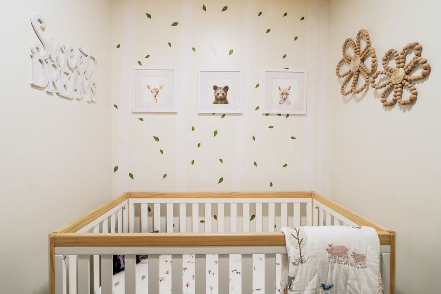 Nursery with wooden crib, animal art, leaf decals, and rope flower decor on a cream wall.