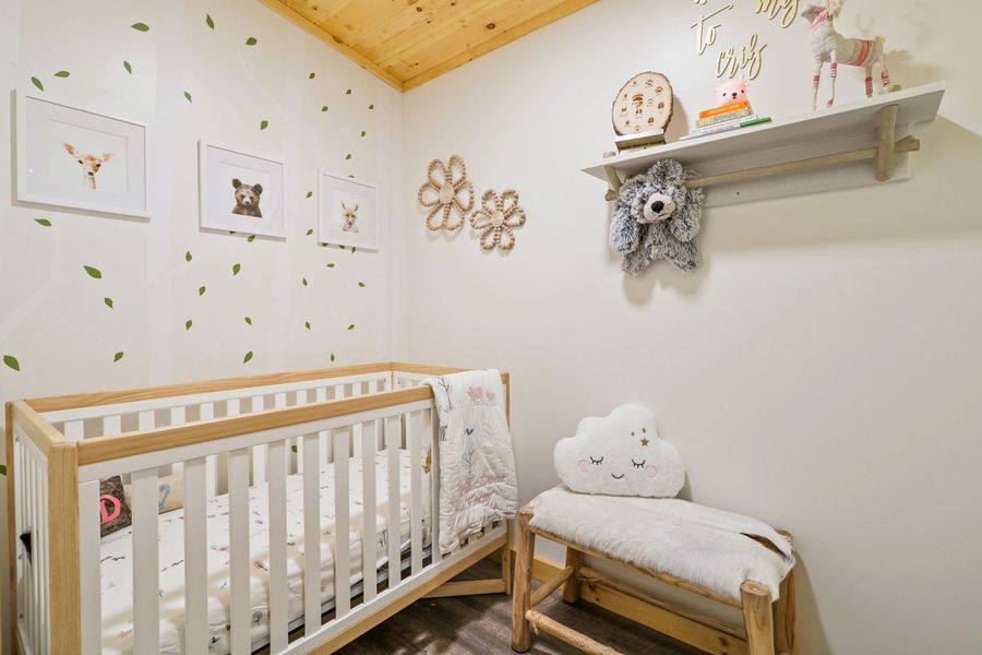A baby's nursery decorated with a woodland theme; features a crib, bench, artwork, and leaves on the wall.