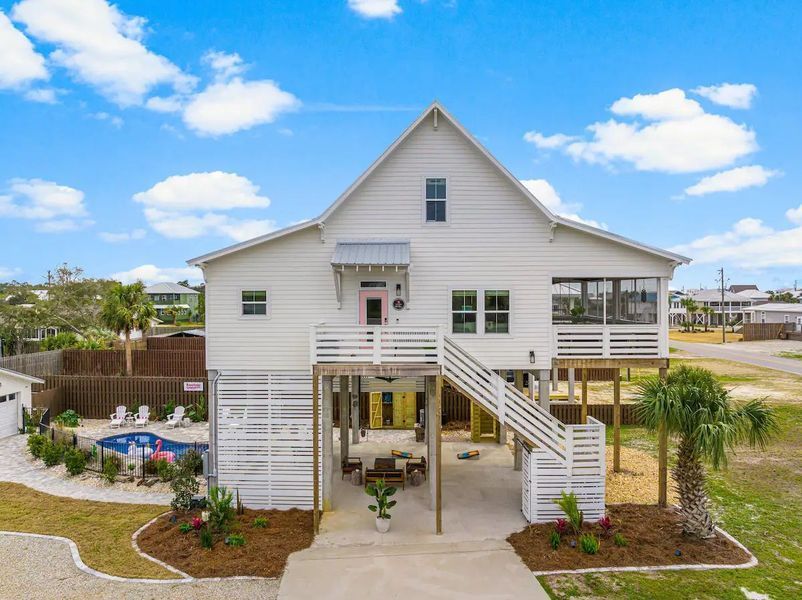 White beach house on stilts with porch and pool, blue sky.