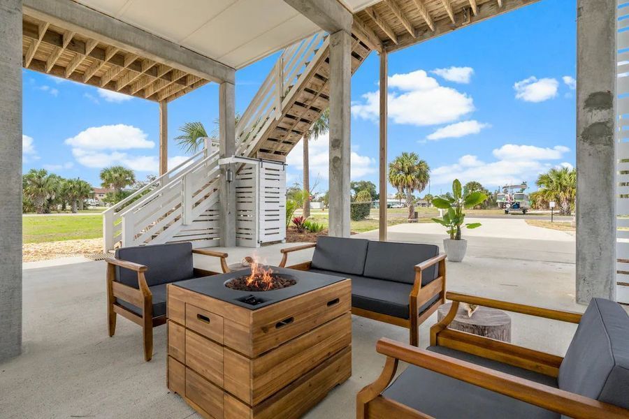 Outdoor seating area under a raised beach house, with fire pit and stairs.
