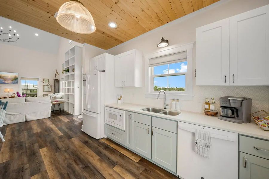 Kitchen with white cabinets, wood ceiling, and view of living area and outdoors.