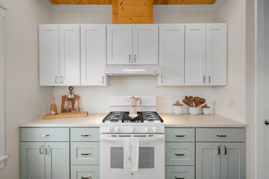 Kitchen with white upper cabinets, blue-green lower cabinets, and a white gas range.