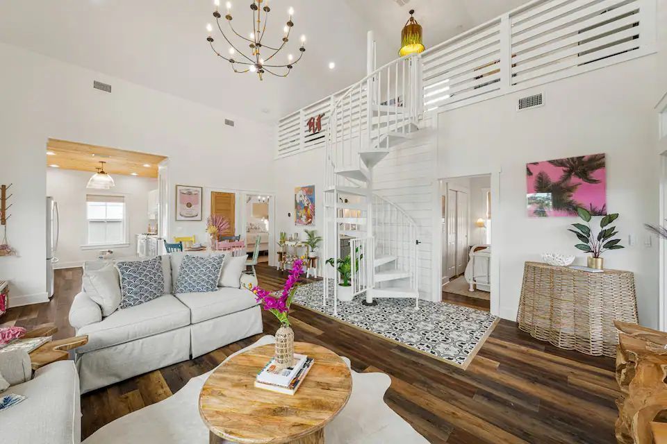 Bright living room with spiral staircase, white walls, wood floors, and colorful artwork.