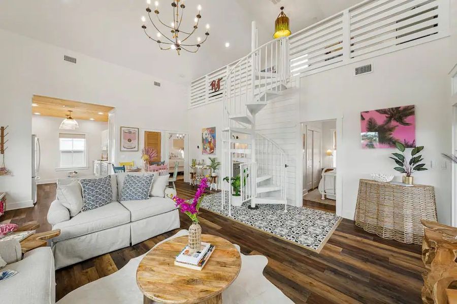 Bright living room with spiral staircase, light-colored sofa, wooden floor, and a round coffee table.
