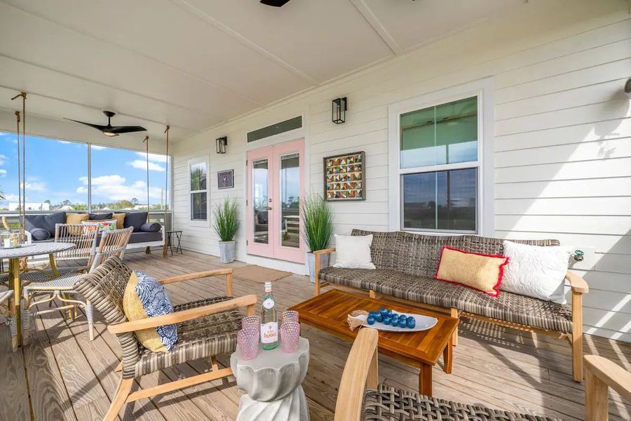 Covered outdoor patio with seating, a table, and pink French doors.