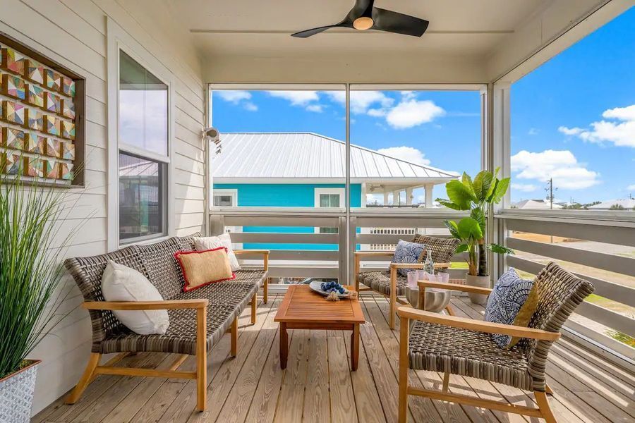 Screened porch with seating, wooden floor, and view of blue house and sky.