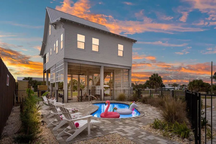 Beach house with pool, chairs, and a flamingo float at sunset.