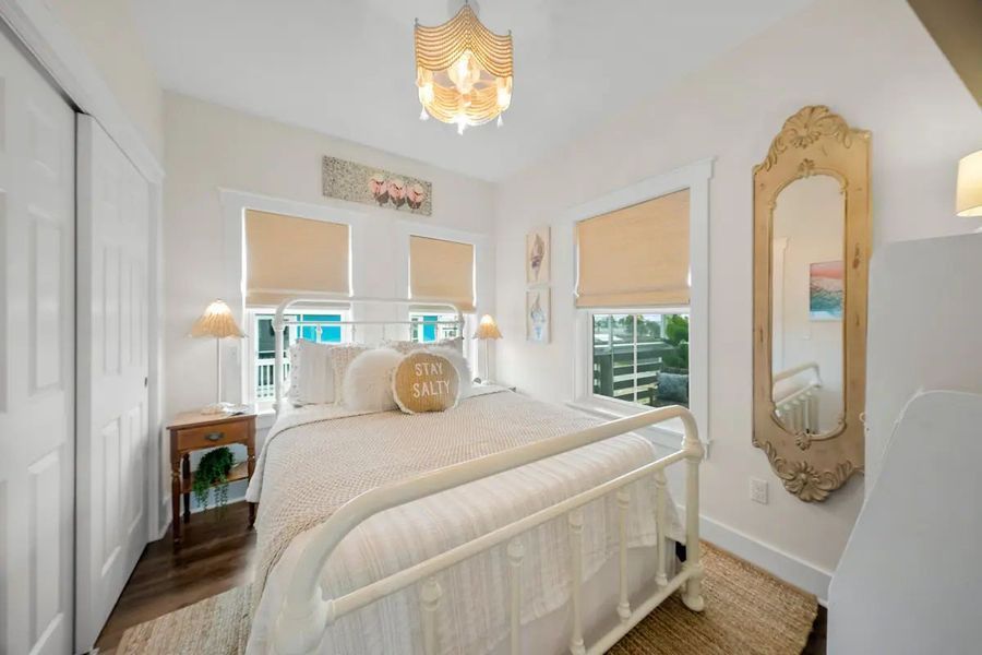 Bedroom with a white bed, matching walls, beige blinds, and a decorative chandelier and mirror.