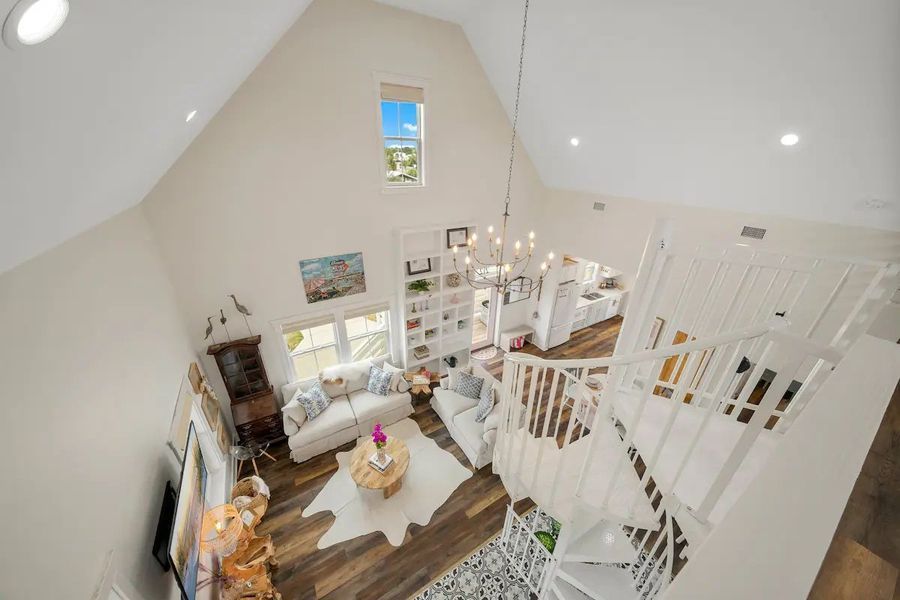 Bright, high-ceiling living room with a staircase. White walls, dark wood floors, and cozy seating areas.