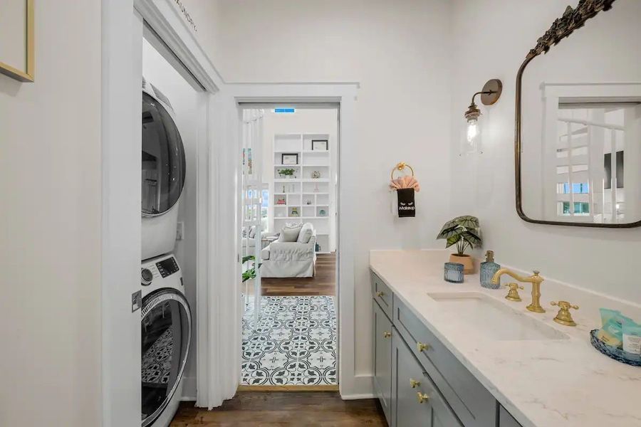 Bathroom interior with stacked washer/dryer, vanity, and a view into another room with shelves.