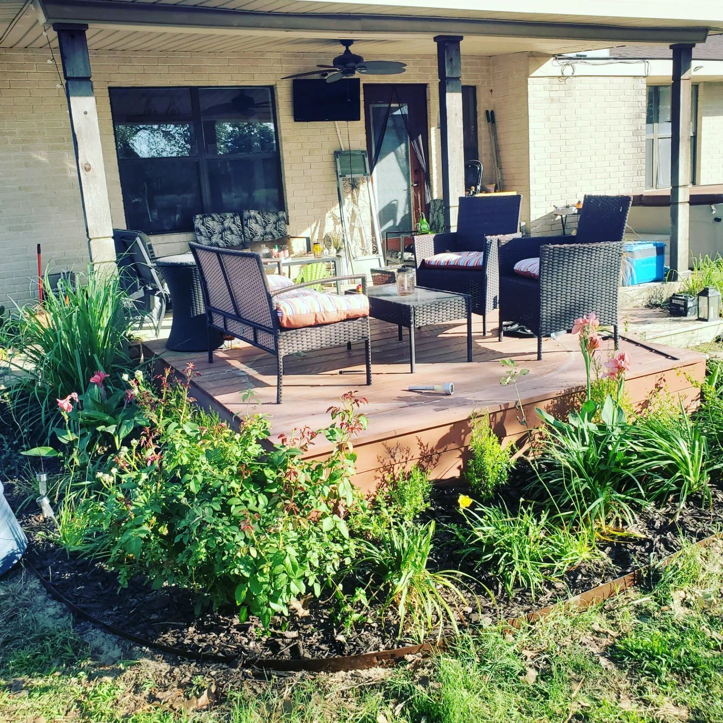 Patio with wicker furniture, brown decking, flower bed in front.