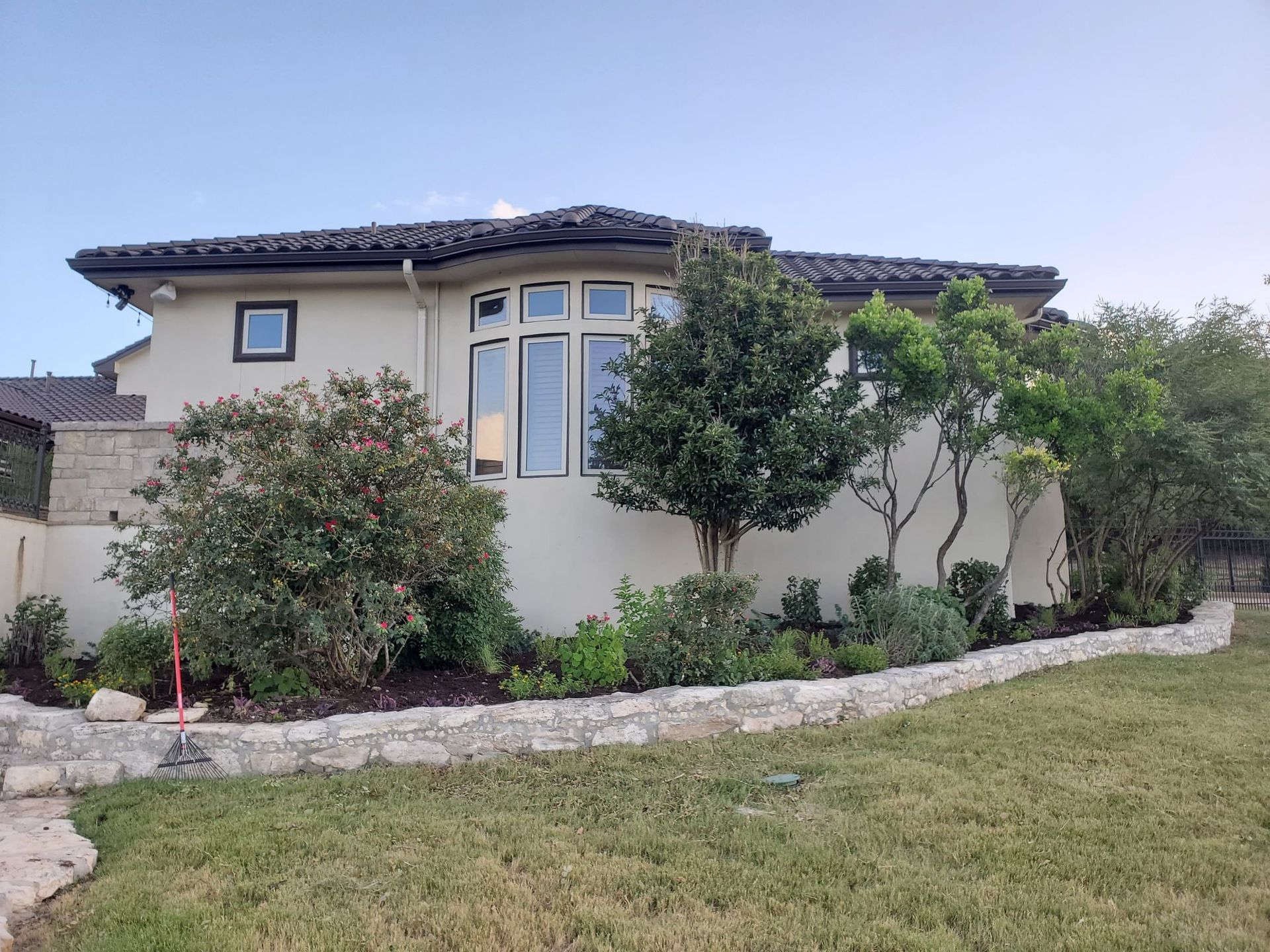 Beige stucco house with dark tile roof and landscaping in front.
