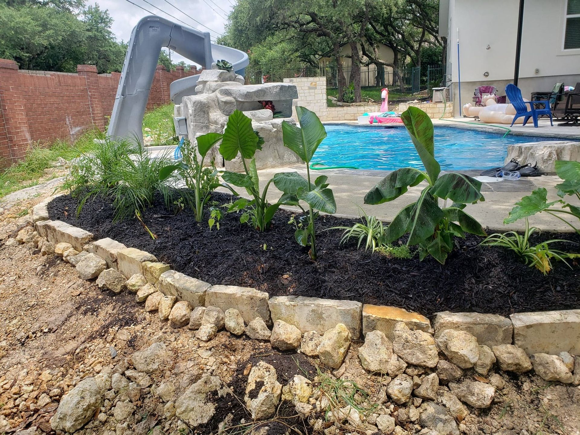 Poolside landscaping with plants and dark mulch, next to a pool with a water slide.
