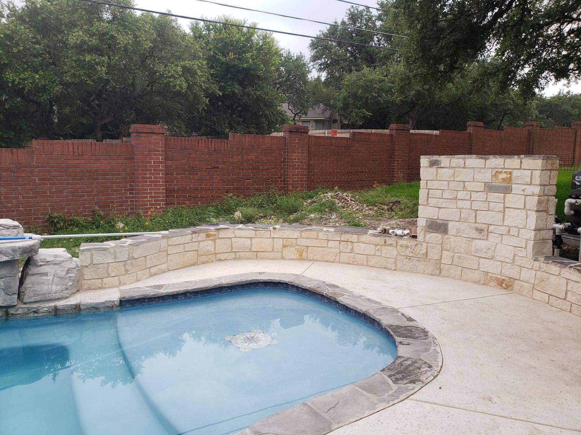Swimming pool with stone trim and red brick wall in the background.