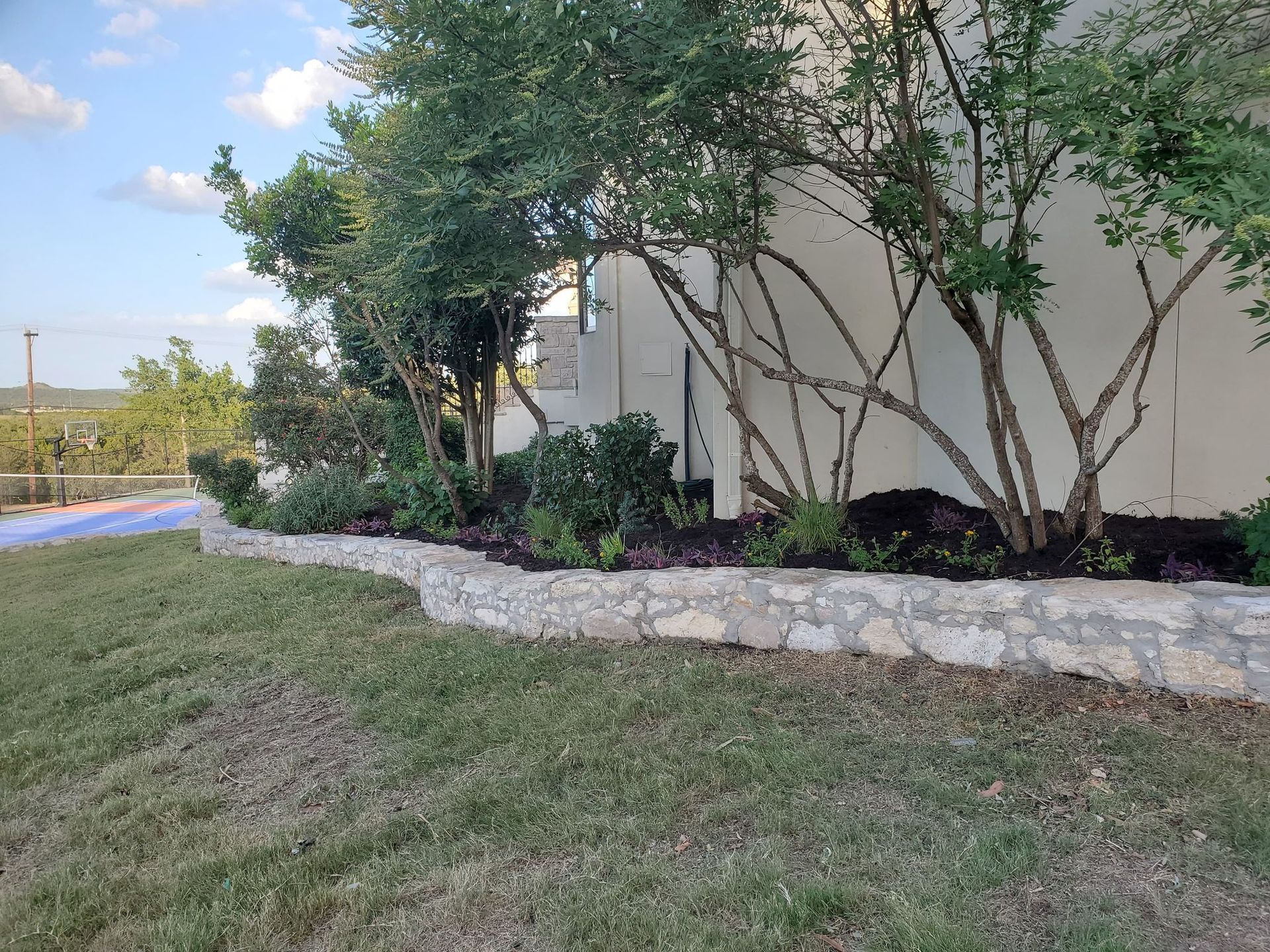 Stone retaining wall with plants in front of a white building, blue sky backdrop.