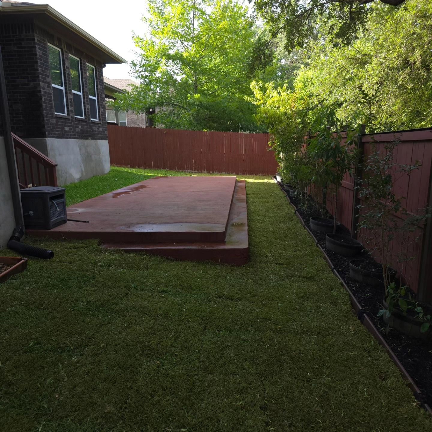Backyard with wooden deck and freshly mowed green grass next to a red fence and house.