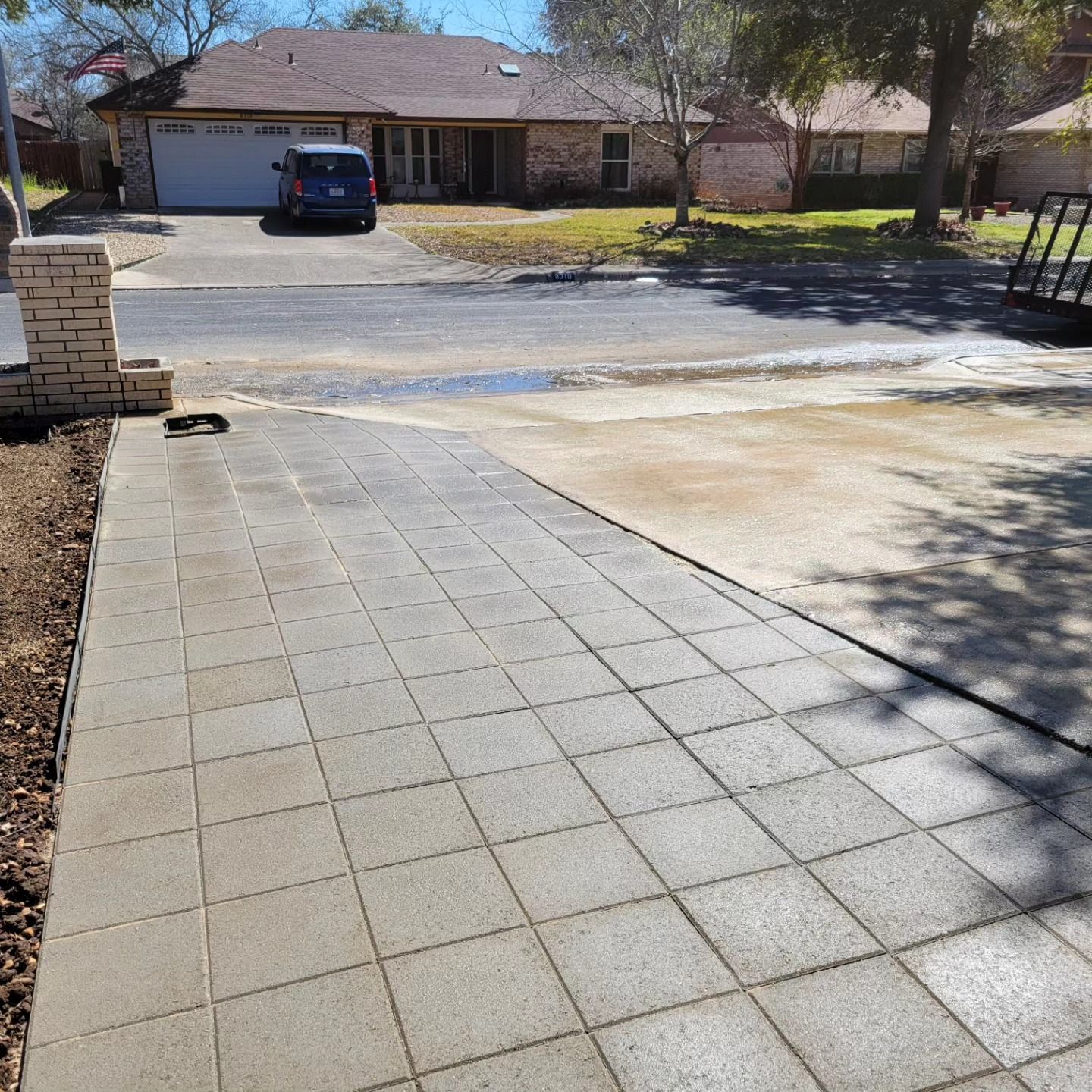 Driveway with gray square pavers leading to a house, with a vehicle parked in front of a garage.