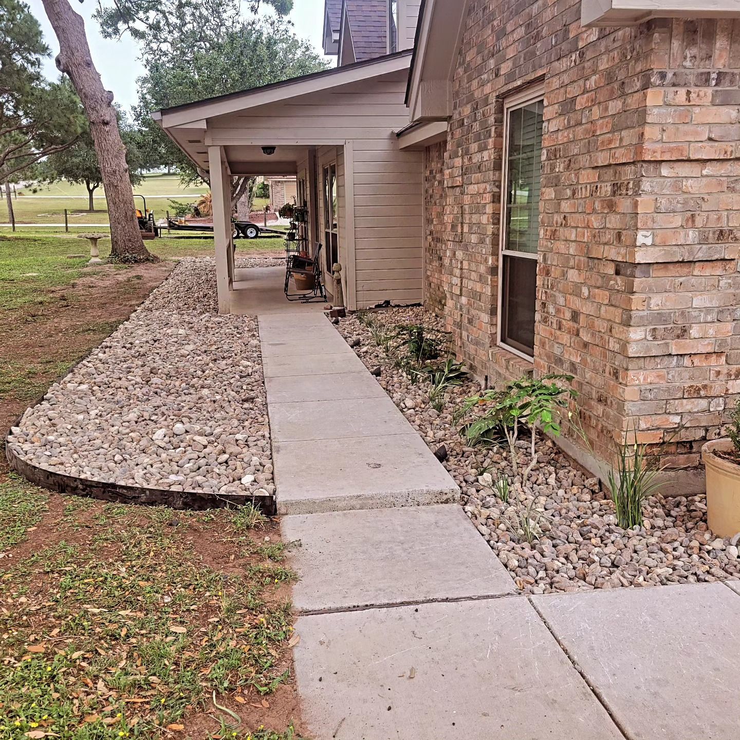A concrete walkway leading to the porch of a brick house with rock landscaping.