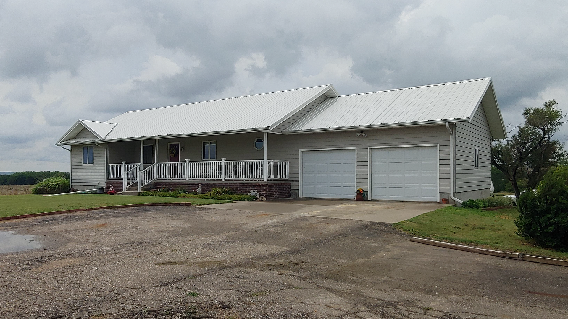 A white house with two garage doors and a porch on a cloudy day.