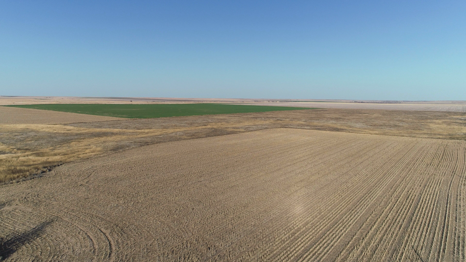 An aerial view of a ploughed field with a green field in the distance.