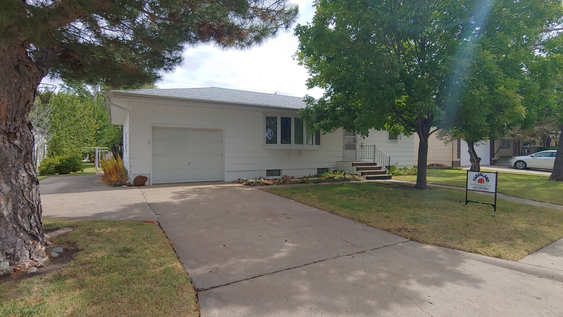 A white house with a garage and a tree in front of it.