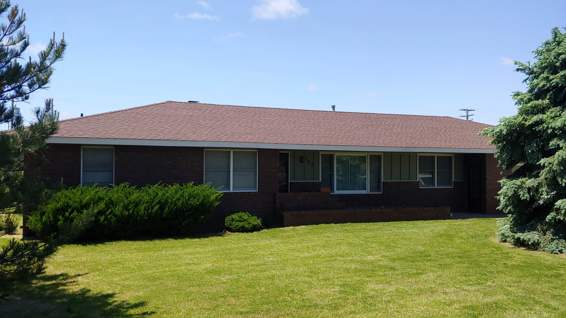 A brick house with a brown roof and a large lawn in front of it.