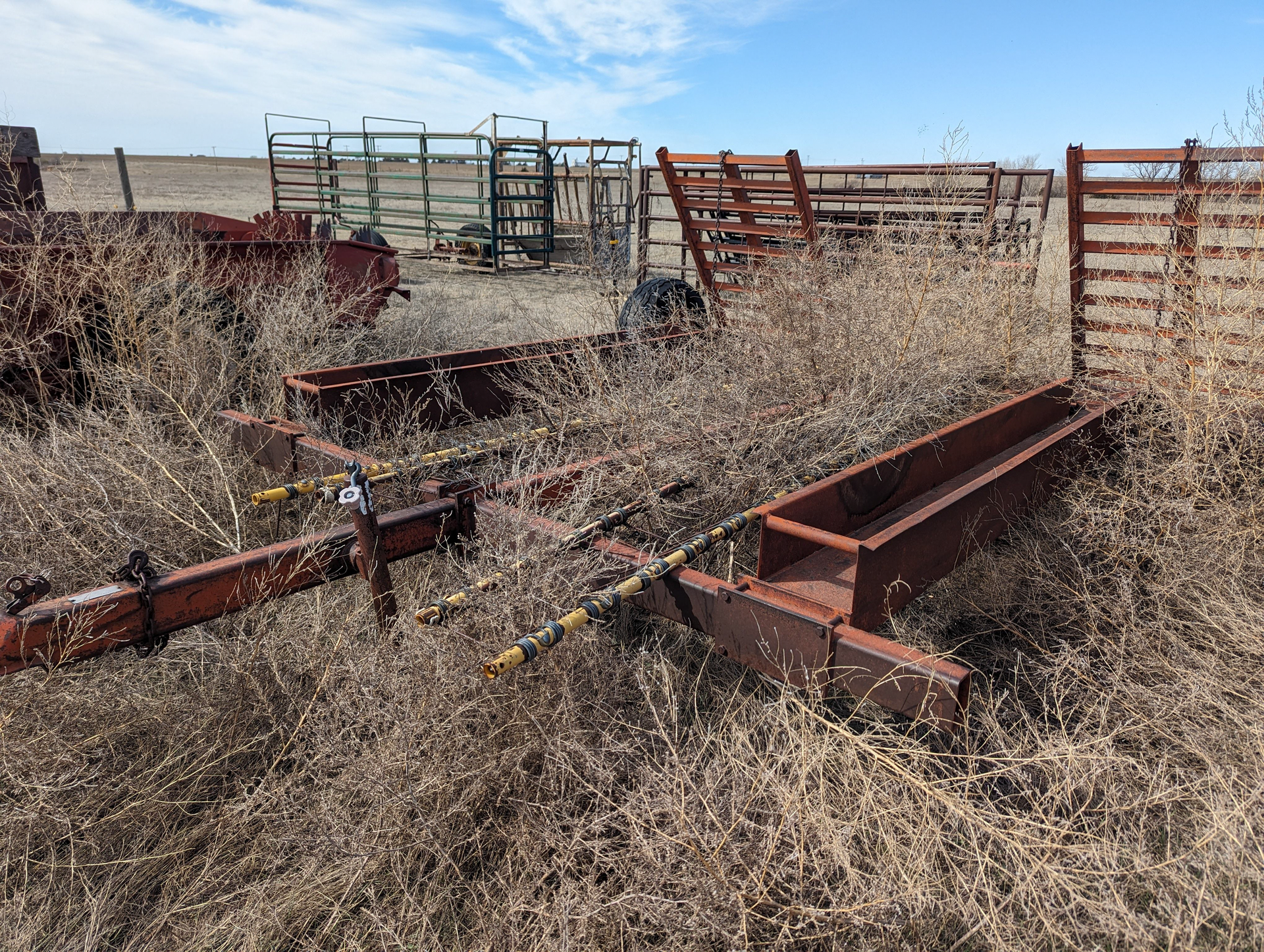 A rusty trailer is sitting in the middle of a dry grass field.