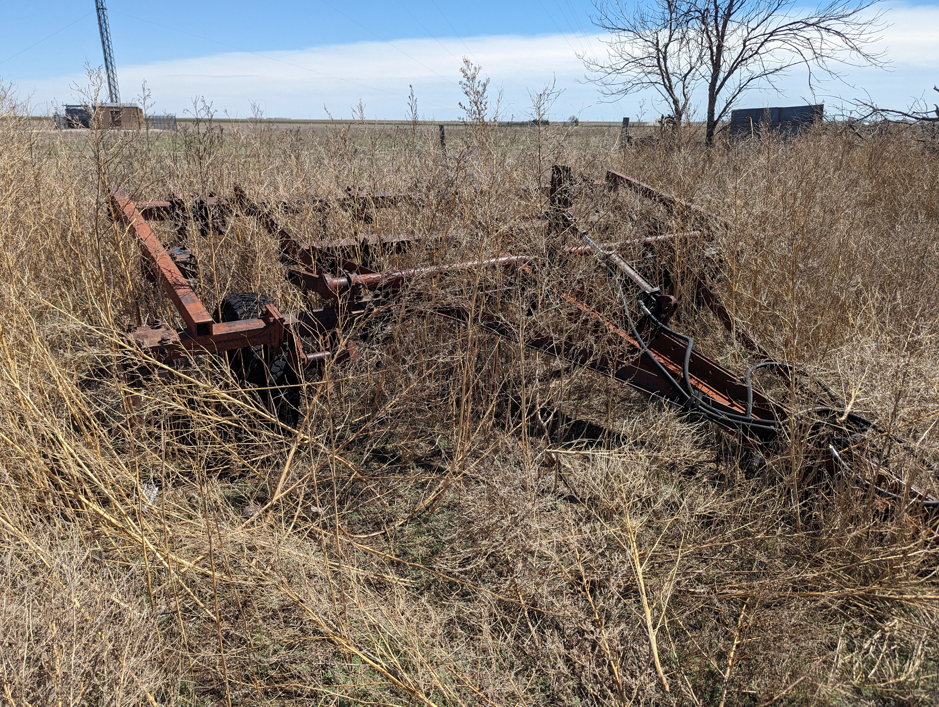 An old rusty plow is sitting in the middle of a dry grass field.