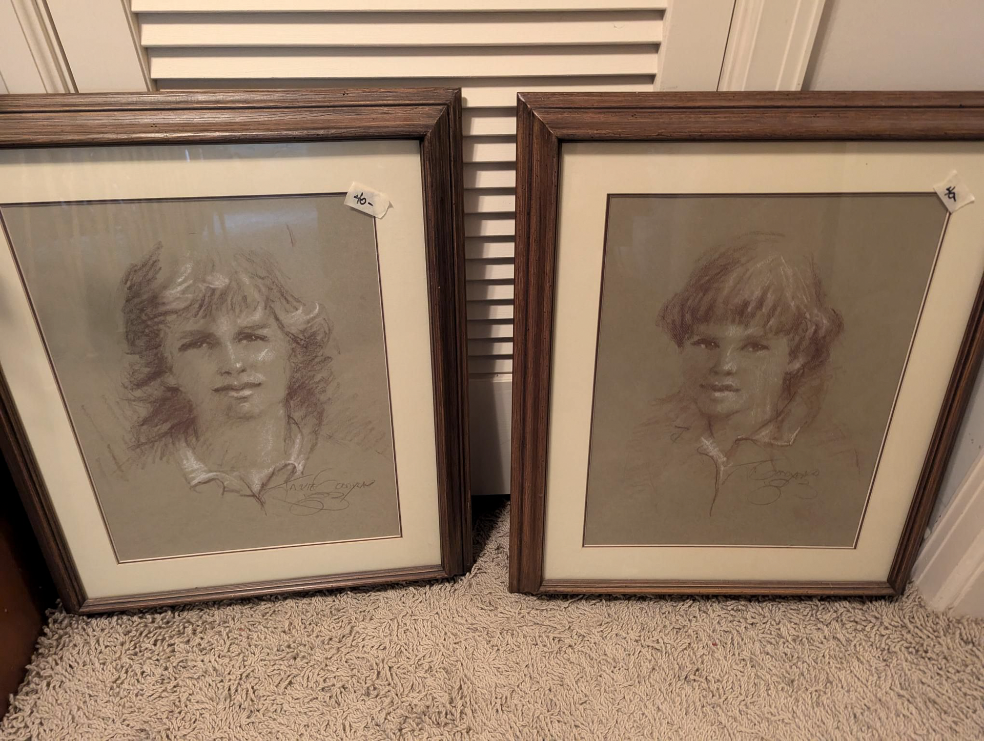 Two framed portraits of a boy and a girl are sitting on a carpet.