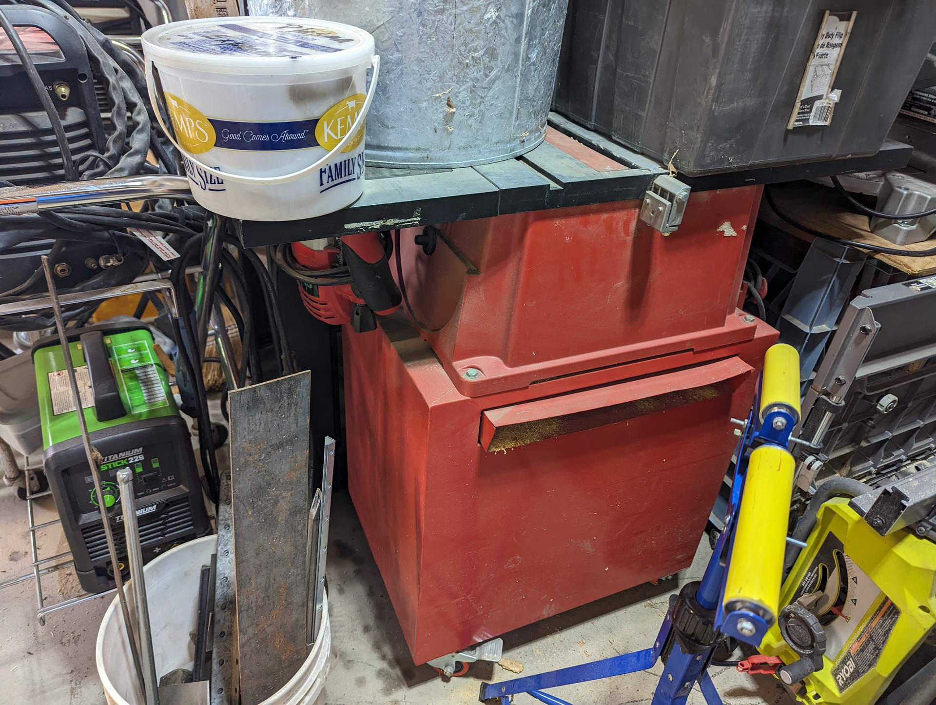 A bucket is sitting on top of a red machine in a garage.