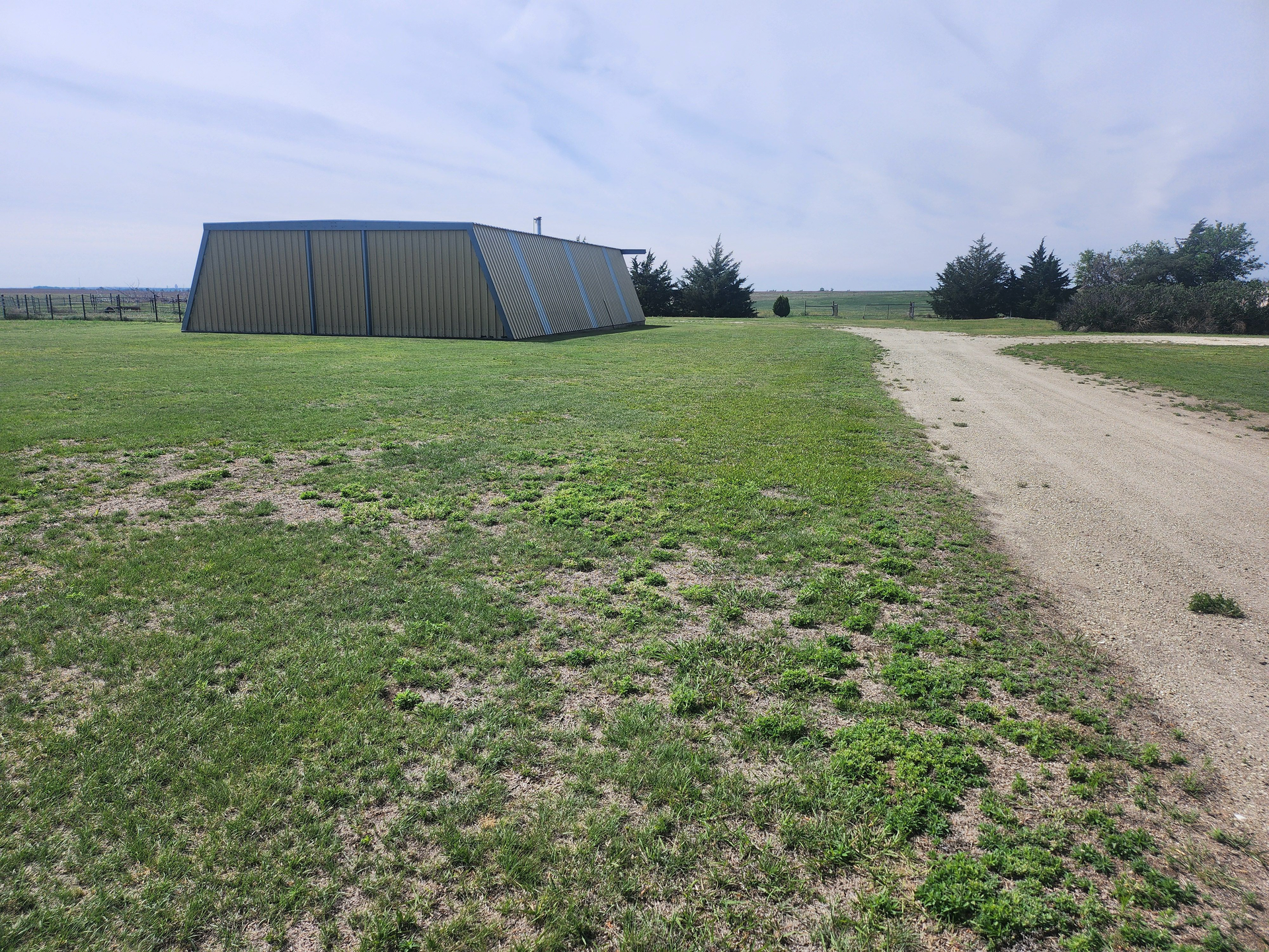 A tent is sitting in the middle of a grassy field next to a dirt road.
