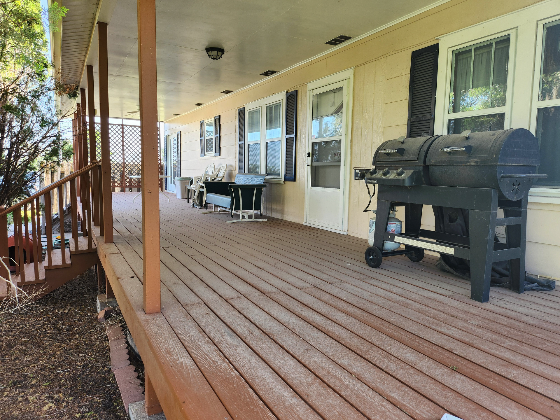 A wooden deck with a grill on it in front of a house.