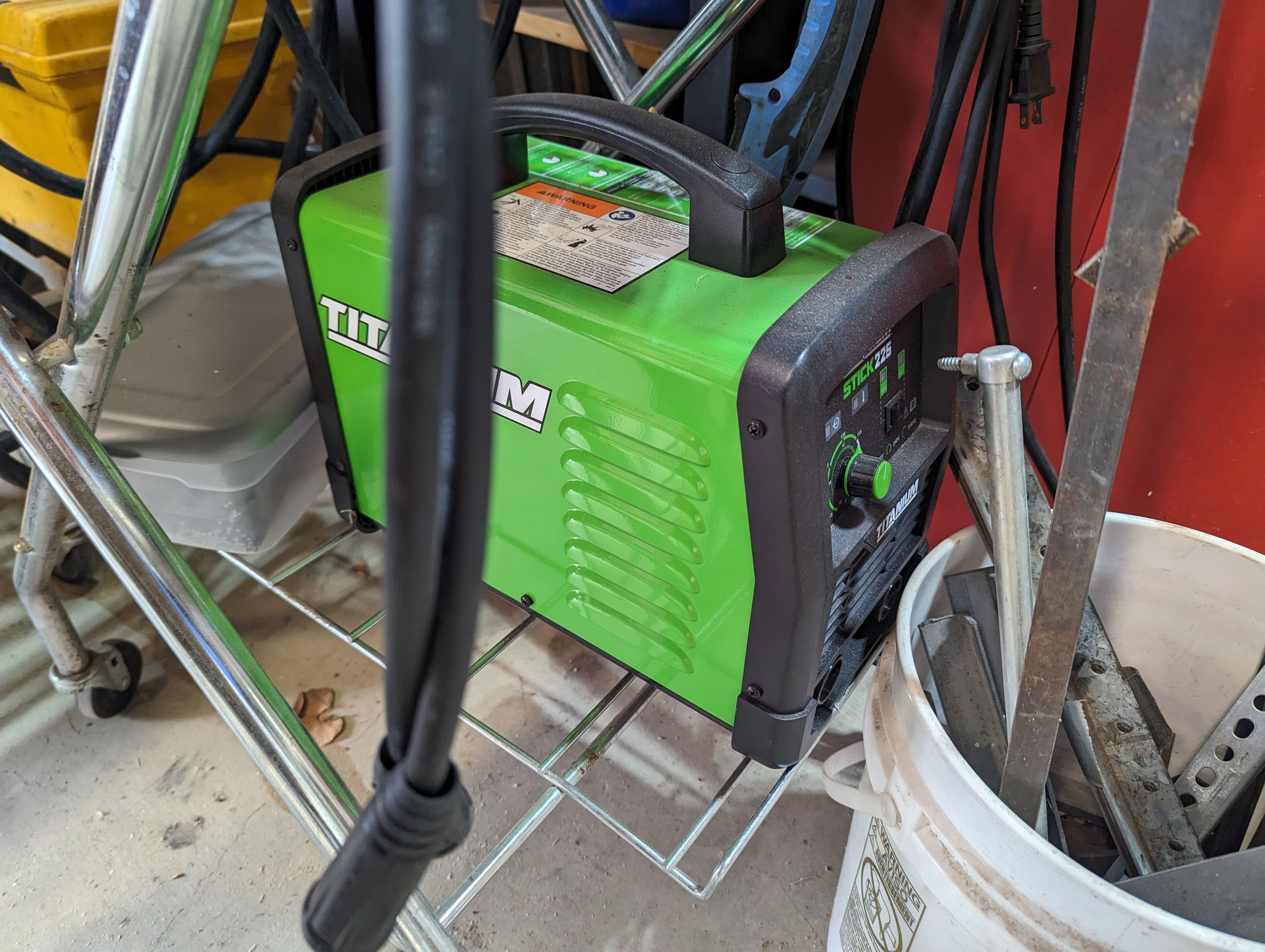 A green and black welding machine is sitting on top of a metal rack.