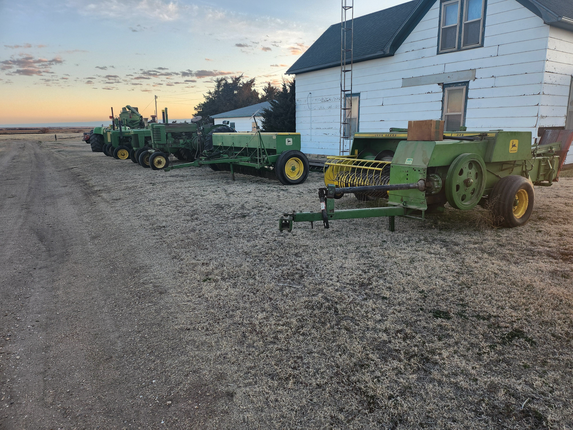 A row of john deere tractors are parked in front of a white house.