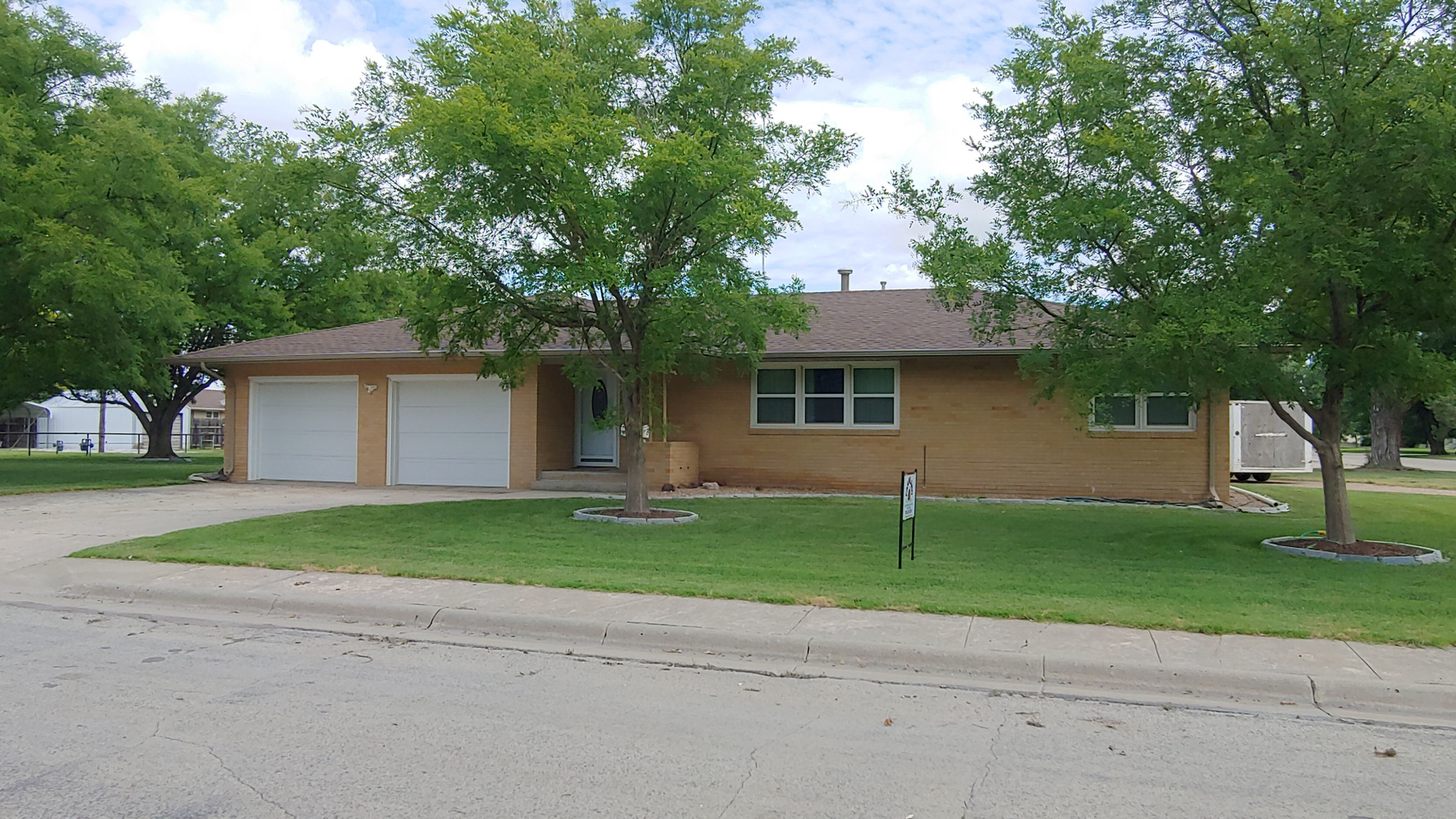 A brick house with two garages and trees in front of it