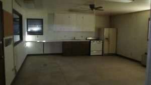 An empty room with a refrigerator , stove , sink and ceiling fan.