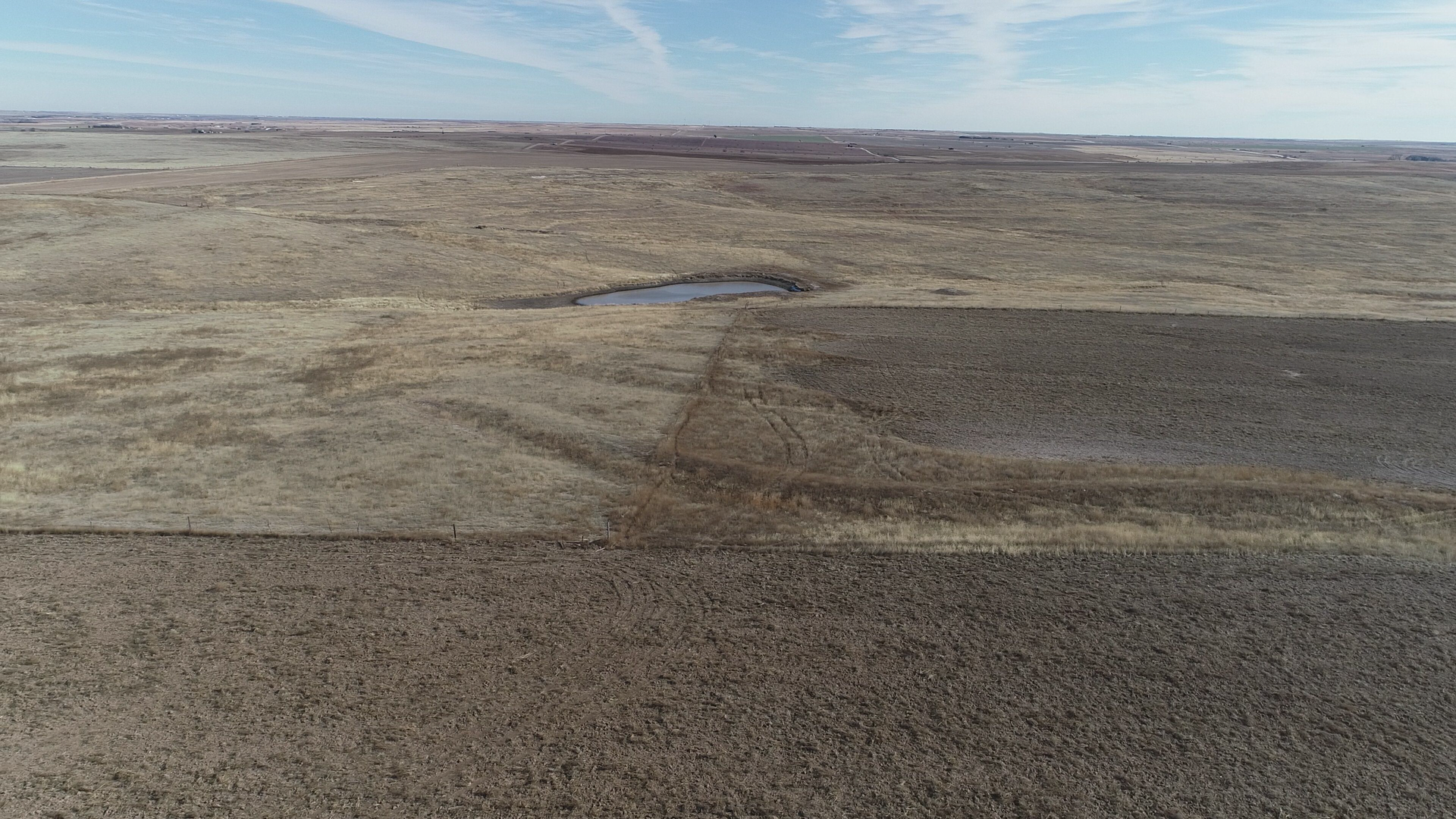 An aerial view of a dry grassy field with a puddle in the middle.