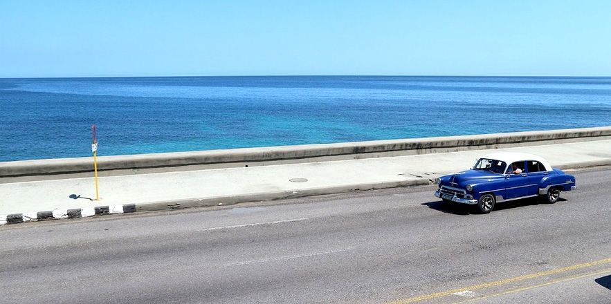 Un coche azul circula por una carretera junto al océano.