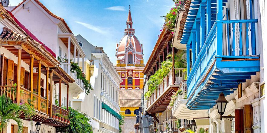 Una calle estrecha bordeada de edificios y balcones con una torre de reloj al fondo.