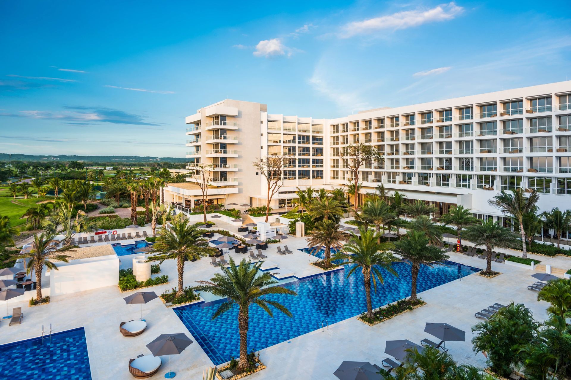 Una vista aérea de un gran hotel con piscina rodeada de palmeras.