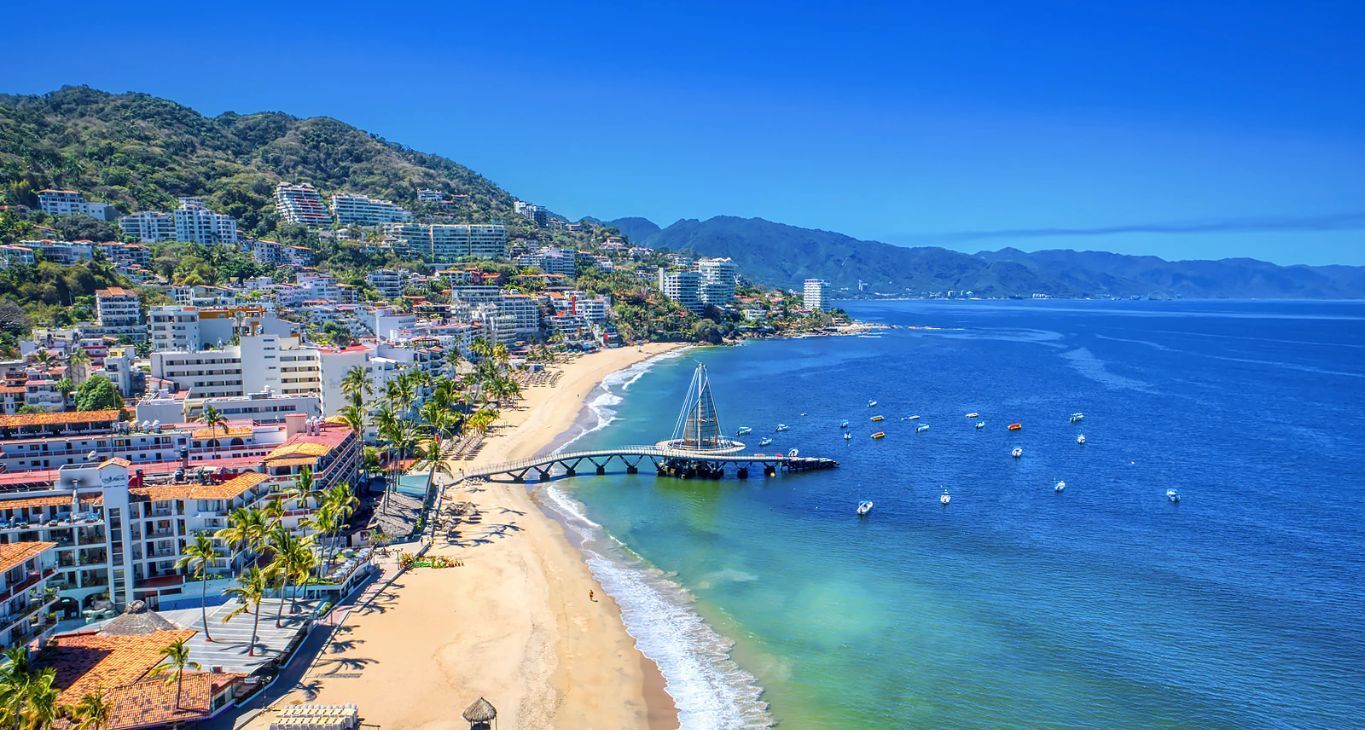 Una vista aérea de una playa con un muelle y una ciudad al fondo.