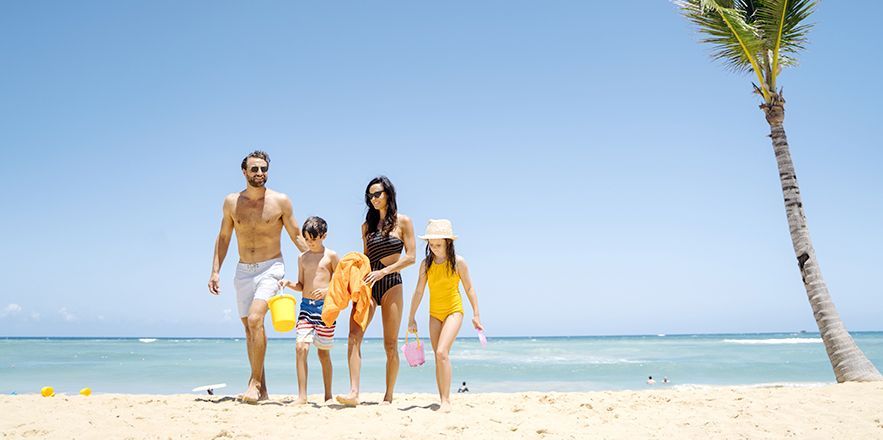 Una familia está parada en una playa junto a una palmera.