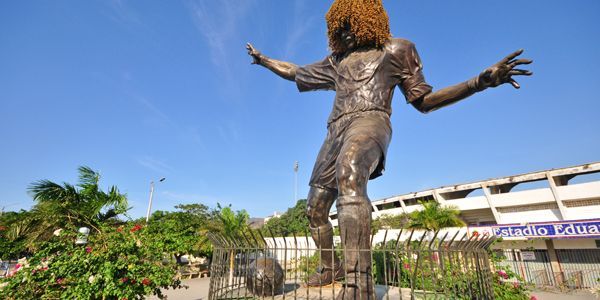 Una estatua de un hombre con cabello rizado está parada frente a un edificio.